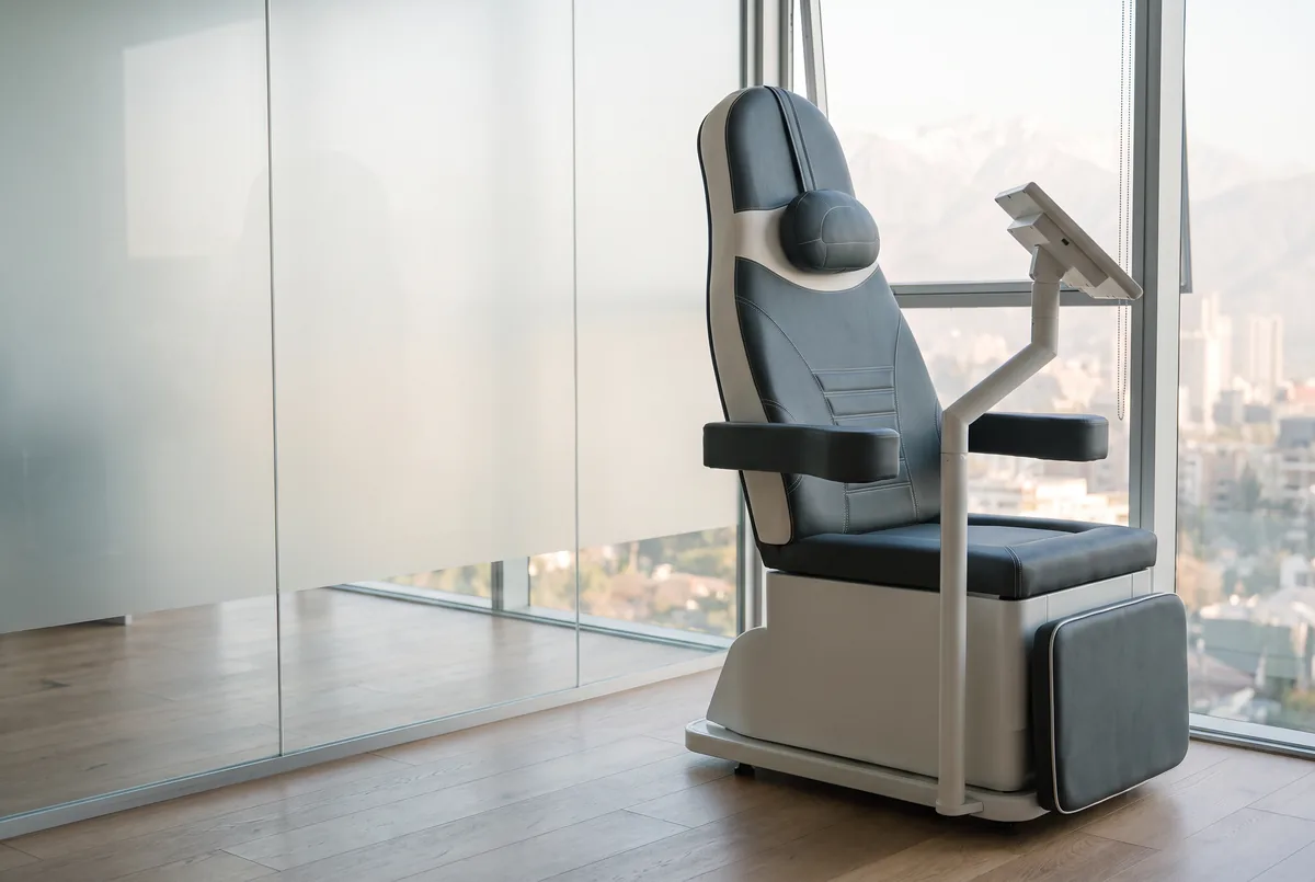 La silla PelviX™ de Spark junto a la ventana: asiento, respaldo con cabezal, apoyabrazos, apoyapiernas, base y brazo con pantalla